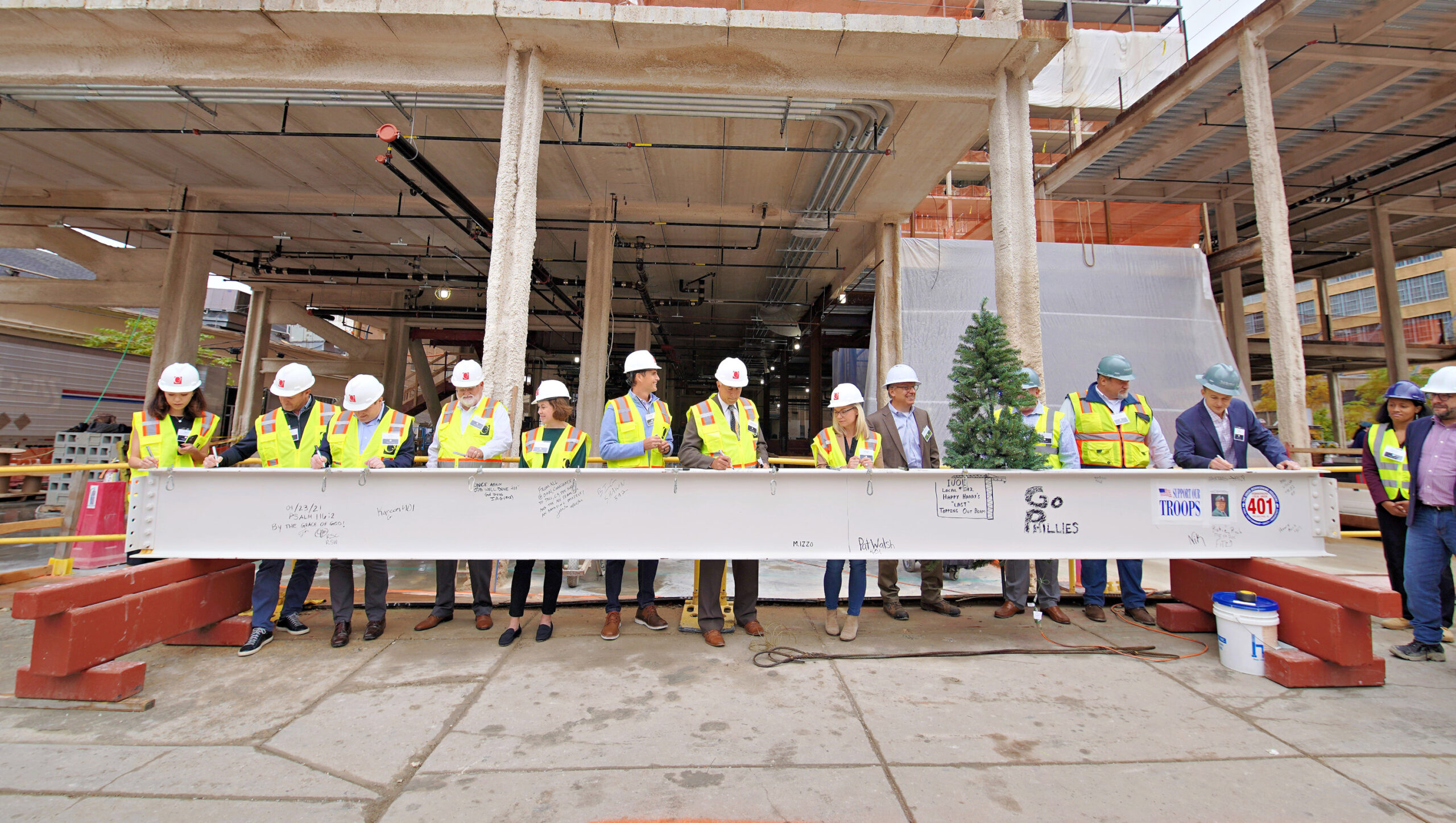 Group of people wearing hard hats signing steel beam