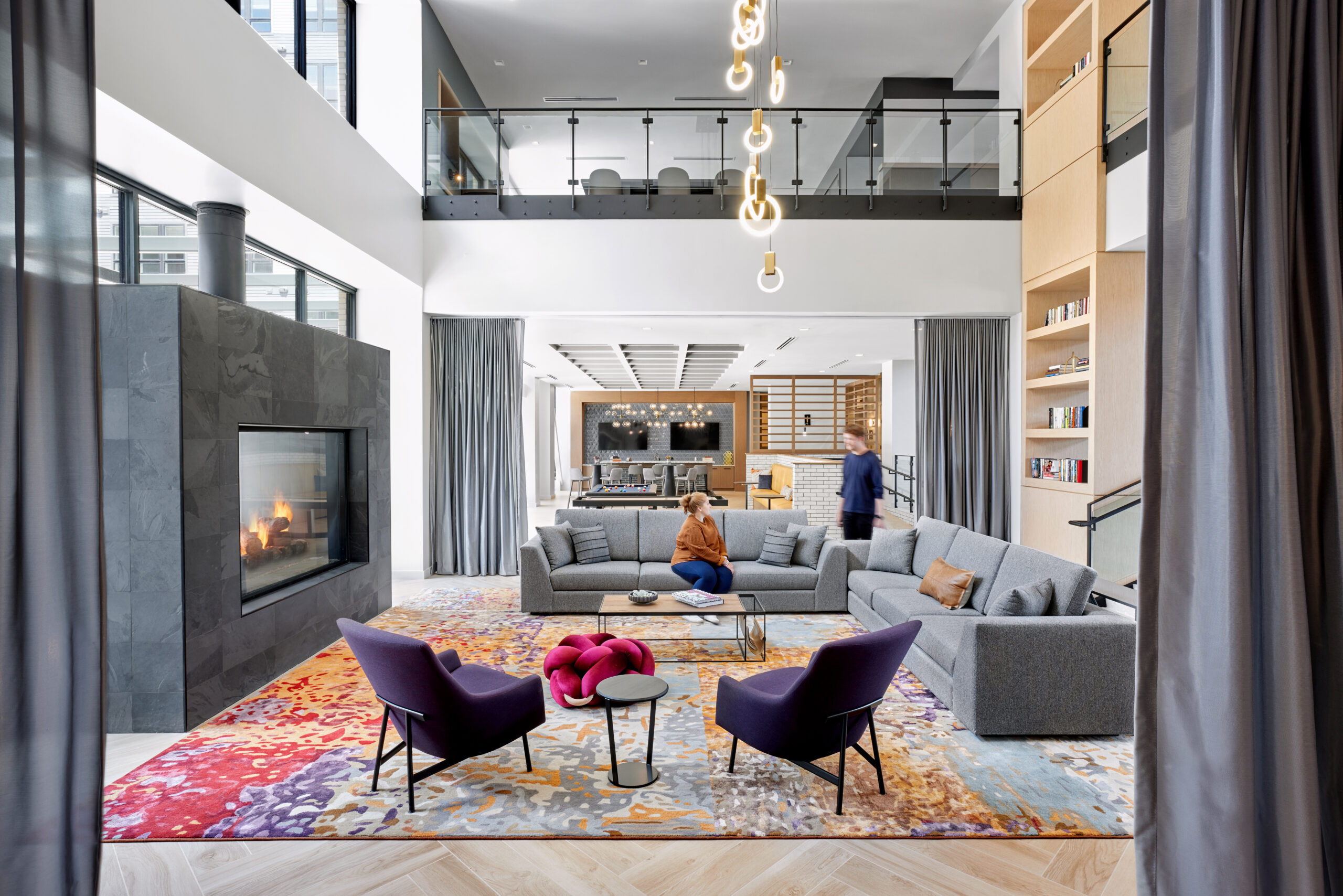 Lounge with gray couches, purple chairs, fireplace and modern chandelier