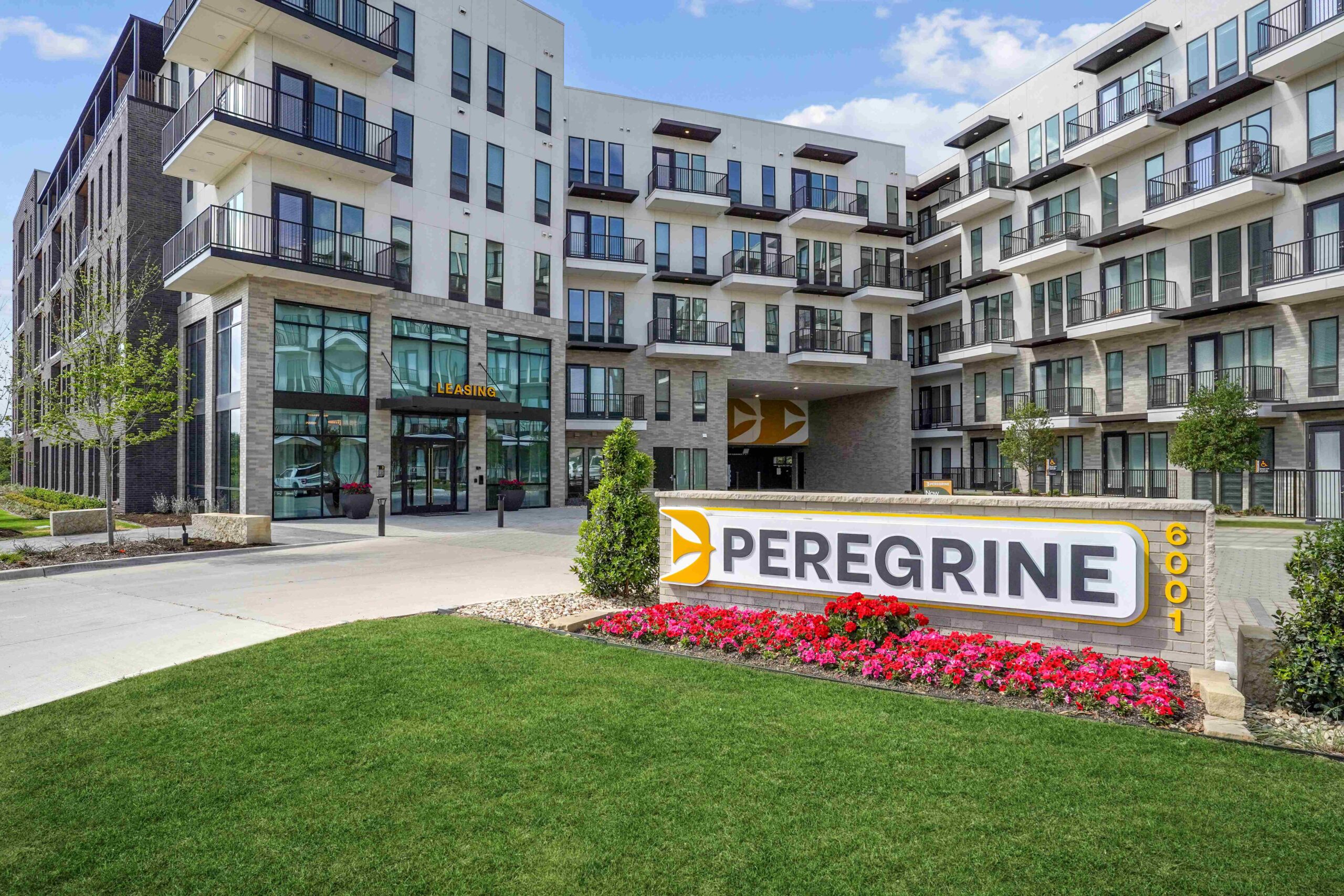 Exterior of an apartment building with balconies and a sign that says "Peregrine" with red and pink flowers beneath it.