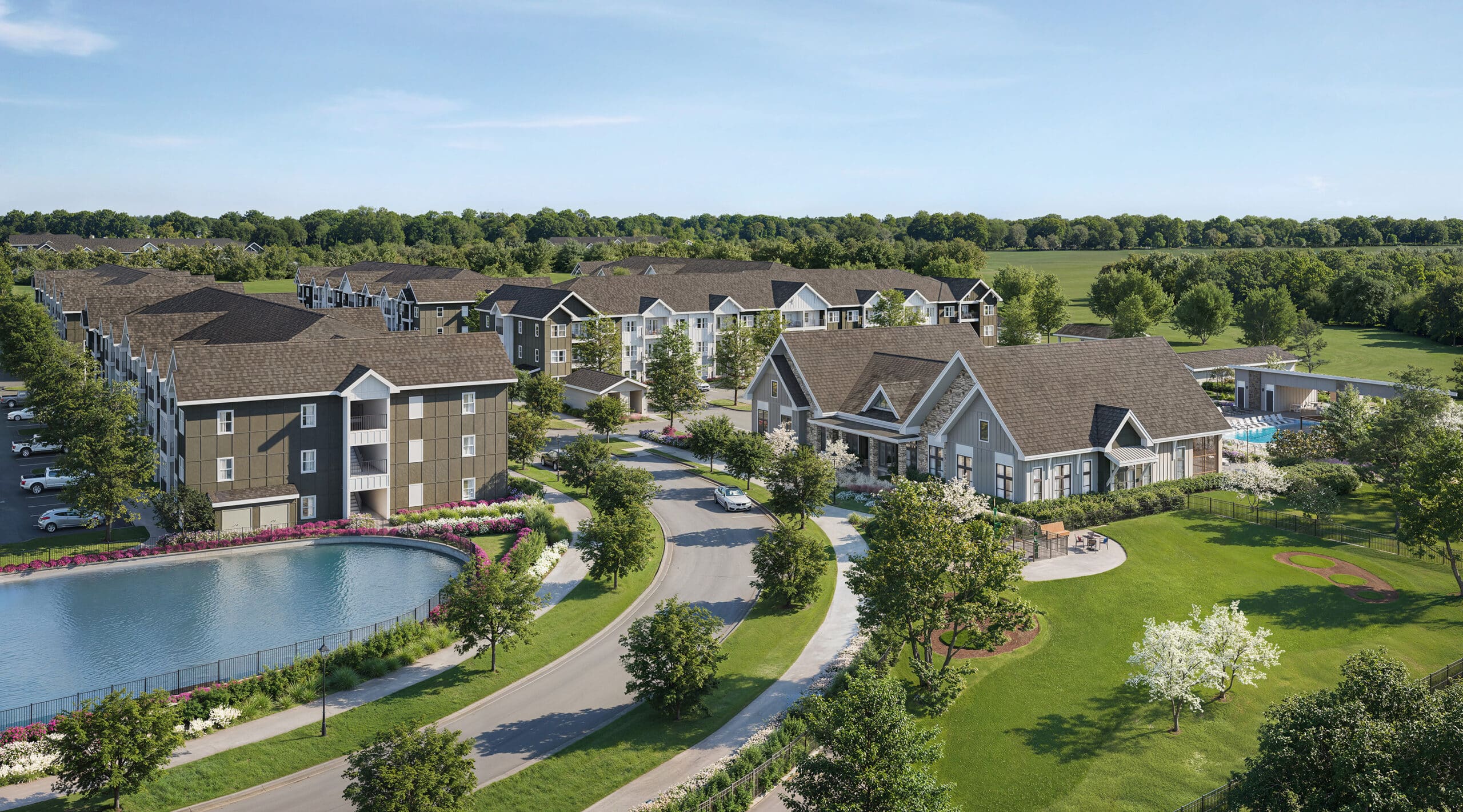 A low-rise apartment community with multiple buildings beige and green walls and brown roof surrounded by greenery and next to a small oval-shaped lake.